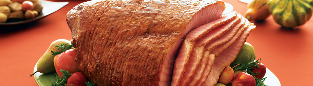 whole cooked ham with half slices on white platter on orange tablecloth