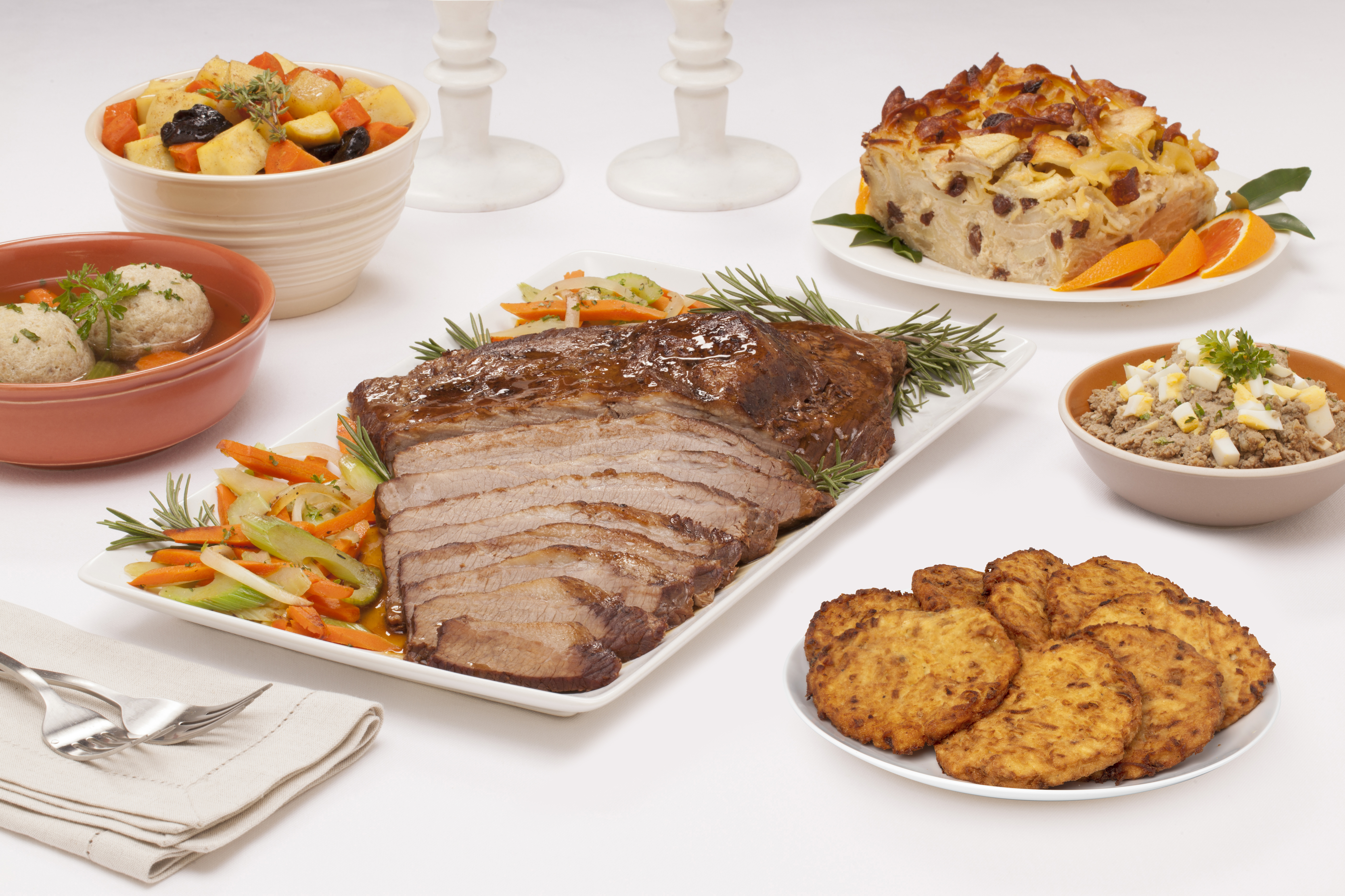 sliced brisket on white plate with vegetables surrounded by side dishes